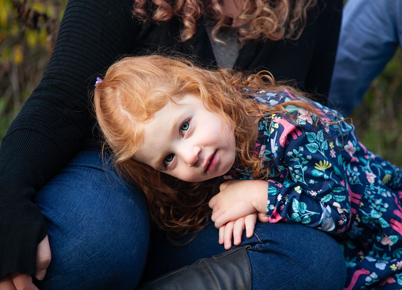 A young girl with red hair leaning on someone's lap