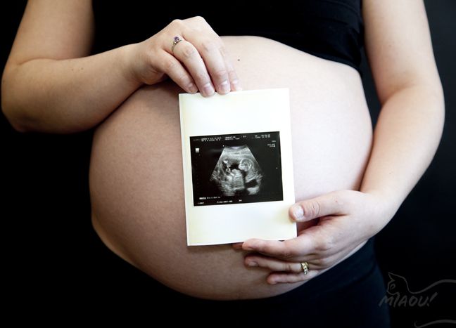 A person with a round, pregnant belly is holding up a black and white ultrasound image