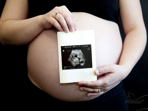 A person with a round, pregnant belly is holding up a black and white ultrasound image