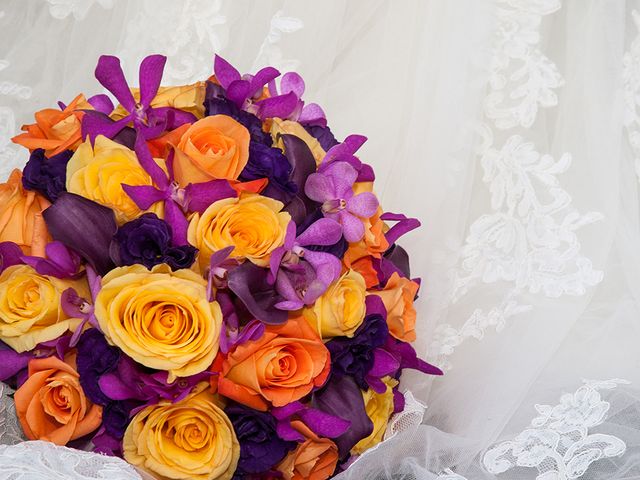 A colorful bouquet of flowers with orange and yellow roses, purple orchids set against a veil with intricate lace patterns.